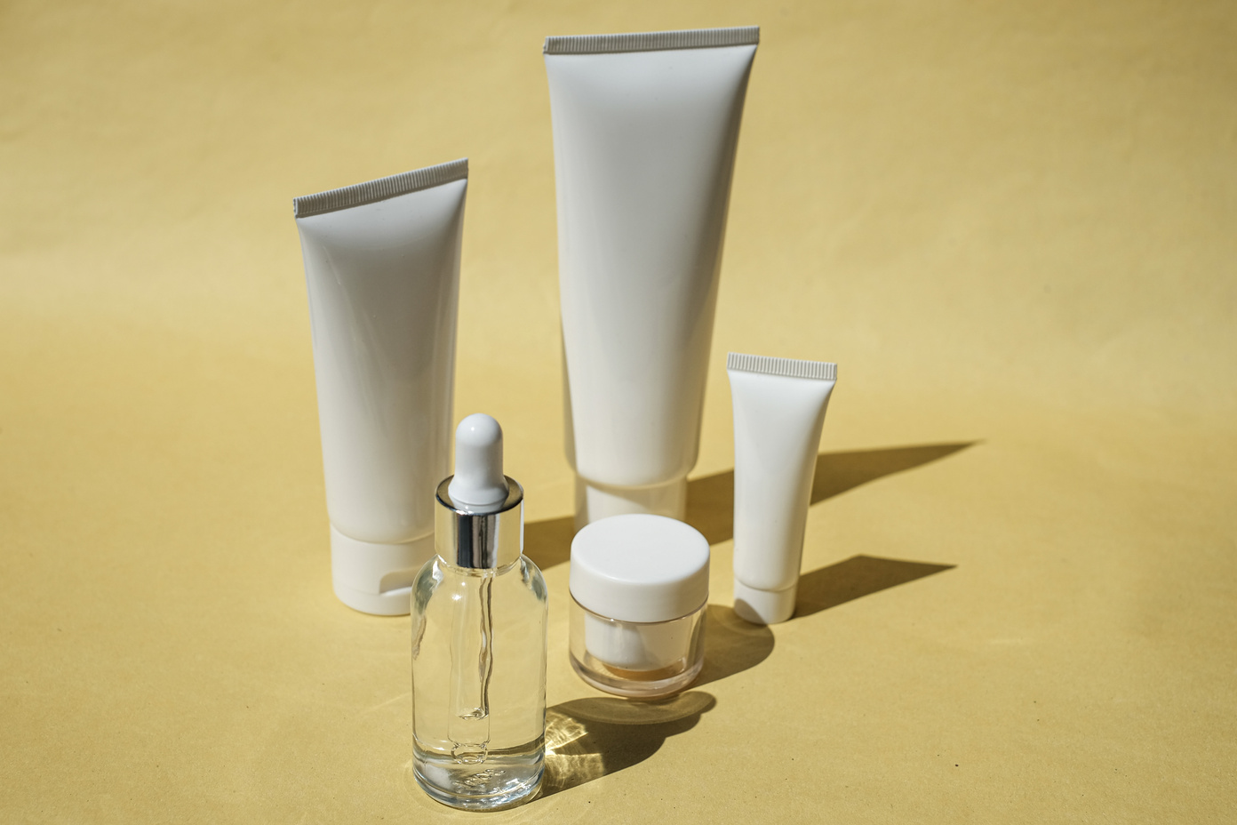 Serum Bottle, Cosmetic Tubes and Container on Yellow Background